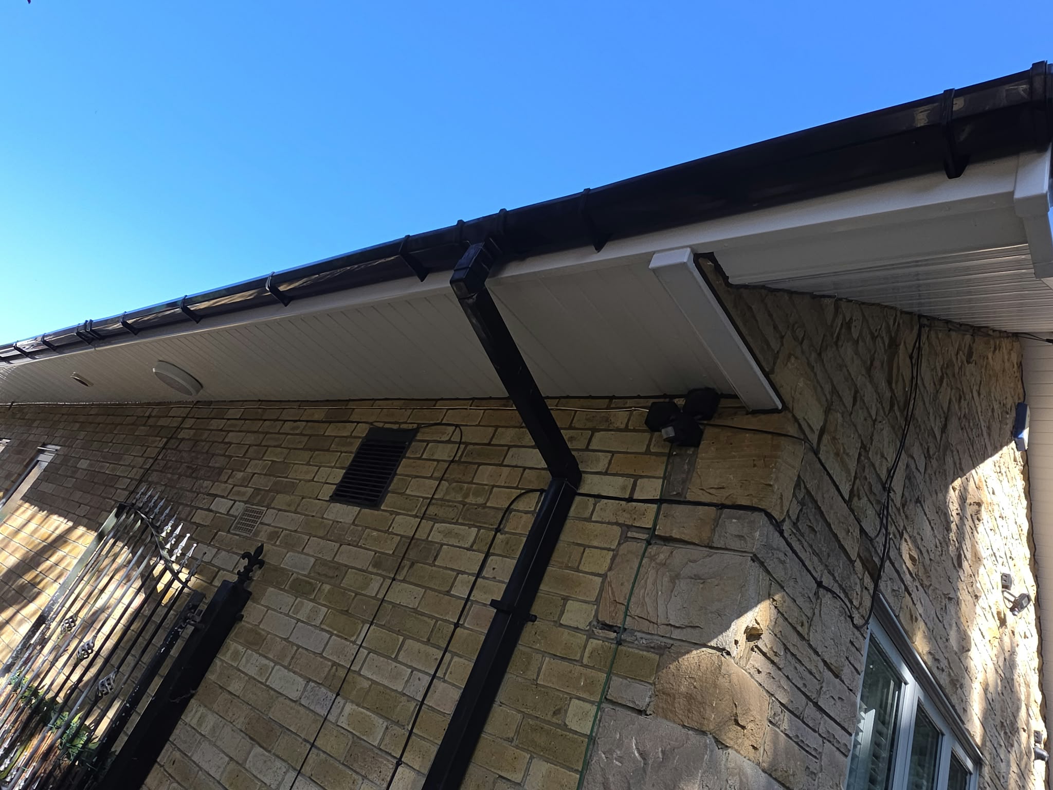 Black external gutter, white soffit and a downpipe at the corner of a brick and stone house